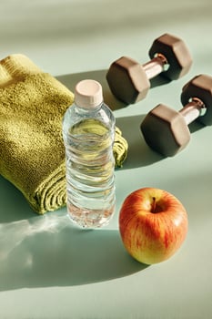 Fitness Essentials on a Pastel Background Featuring a Green Apple, Towel, Water Bottle, and Dumbbell. photo