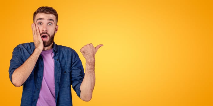 Promotion concept. Shocked hipster guy in casual outfit pointing aside at free space, recommending something, offering huge sale on orange studio background, banner design photo