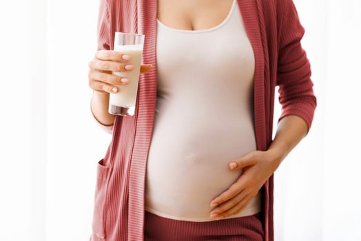 Dairy Products During Pregnancy. Closeup Shot Of Pregnant Lady Holding Glass Of Milk, Unrecognizable Expectant Mother Standing Near Window At Home And Embracing Her Belly, Cropped Image, Free Space photo