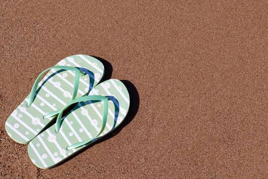 A pair of green flip-flops with white daisy patterns lies on warm golden sand. The image captures a peaceful summer vibe, perfect for vacation or travel themes. photo