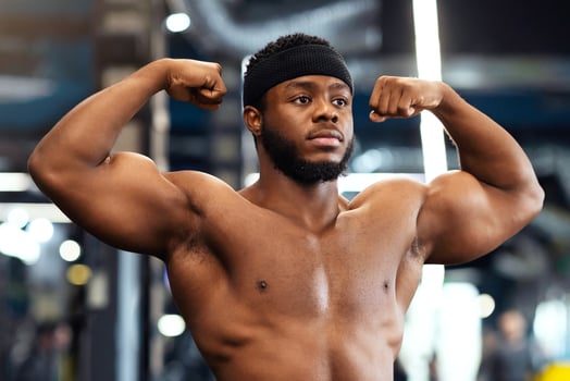 Athletic african american handsome shirtless man posing and showing muscles biceps in gym, looking at copy space. Bodybuilding, powerlifting, health, fitness, active lifestyle concept photo