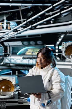 Astronaut using laptop to confirm suit integrity and update flight log. Orbital station crew member testing gear during routine equipment check using notebook, verifying navigation coordinates photo
