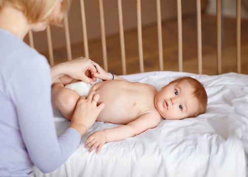 Beautiful baby boy looking at camera while his mother changing nappy, baby girl woke up after nap, laying in wooden baby crib. Mom changing diaper for her little kid, cropped, copy space photo