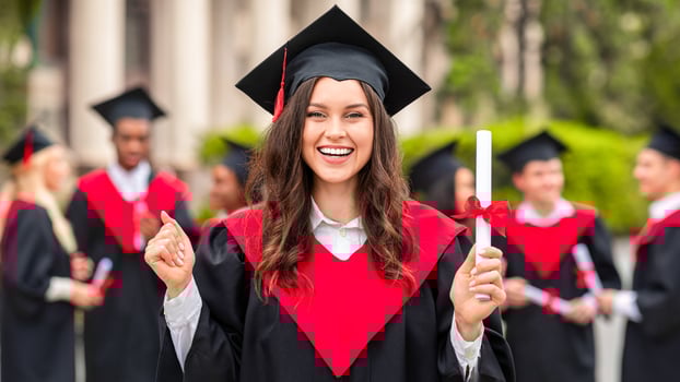 Emotional young woman student having graduation party, wearing graduation robe and hat, holding diploma and cheerfully screaming at camera, posing over international group of graduates photo