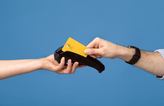 Cropped view of young man making credit card payment on money terminal over blue studio background, closeup of male and female hands. Contactless payment during coronavirus pandemic concept photo