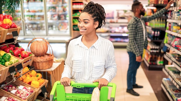 African American Lady Buying Fresh Organic Fruits And Vegetables Doing Grocery Shopping Walking With Shop Cart In Supermarket Indoors. Customer Of Groceries Store Choosing Healthy Natural Food photo