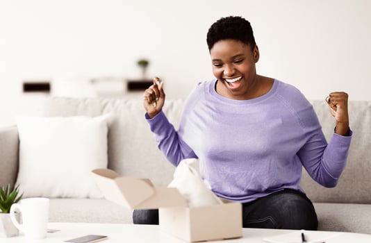 Yes. Emotional black female buyer customer received long-awaited package, shaking clenched fists, opening cardboard box at home, satisfied with great purchase. Reliable postal courier service concept photo
