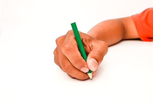 Hand holding a green colored pencil and writing on a white surface or drawing photo