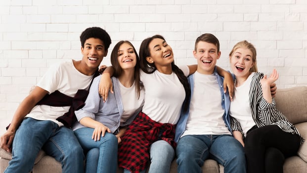 Teen friends sitting on sofa and embracing, smiling together to camera over light wall photo