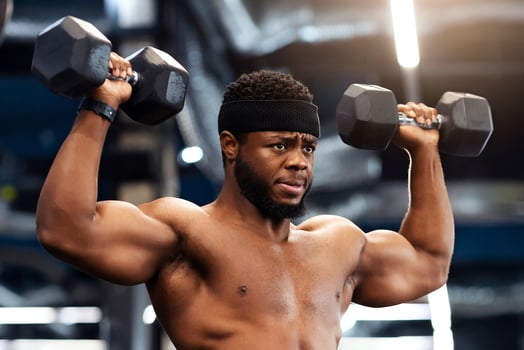 Confident african american shirtless man bodybuilder with muscular body exercising at gym, lifting up dumbbells, making work out for his biceps and back, looking at copy space photo