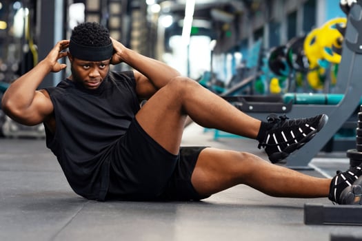Black guy sportsman doing abs on floor in gym, african american muscular young man bodybuilder doing crunches or sit-ups, working on six-pack abs, panorama with copy space, side view photo