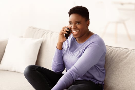 Informal Call. Portrait of emotional young curvy african american woman talking on her smartphone, sitting on the couch in living room at home, discussing news. Distance Communication Concept. photo