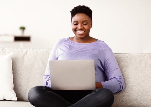 Joyful african american young curvy lady sitting on couch at home, using laptop, watching videos online, chatting with friends or reading blogs, copy space. Rest At Home, Relax And Lifestyle photo