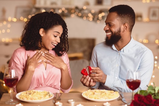 Will You Marry Me. Handsome bearded african american man holding and showing open box, offering marriage ring to his happy fiance, getting engaged in restaurant or at home during romantic date photo