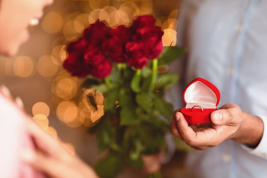 Will You Marry Me. Closeup of unrecognozable african american man showing open box, offering marriage ring to his happy fiance, getting engaged during romantic date, holding bouquet of red roses photo