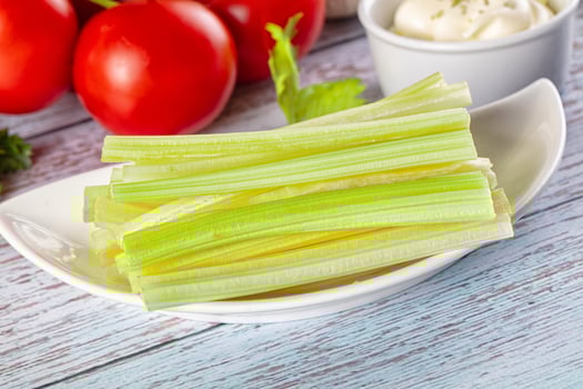 Celery sticks on a white plate with a bowl of sour cream photo