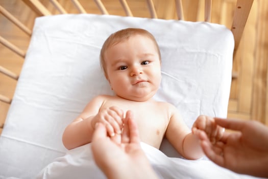 Good morning sunshine. Beautiful little baby laying in cot, holding mom's hands, ready to wake up. Top view of cute blonde toddler waking up, lying in wooden baby bed, grabbing mother fingers photo