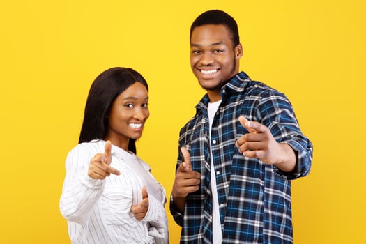 Your turn, you are cool and challenge. Happy excited millennial african american students man and lady in casual show fingers at camera, isolated on yellow background, empty space, studio shot photo