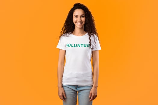 Volunteer Woman Wearing White T-Shirt Standing Smiling To Camera On Yellow Background. Female Activist Posing In Studio. Charity And Volunteering Work Advertisement Banner photo