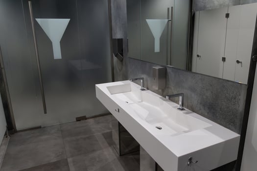 A spacious bathroom showcases a sleek, modern sink with dual faucets and a minimalist aesthetic. Frosted glass partitions add privacy, creating a contemporary atmosphere for users photo