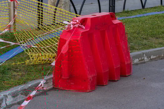 A vivid red plastic barrier stands prominently on the roadside, cordoned off with caution tape as workers prepare for upcoming construction. Sunlight illuminates the area, enhancing visibility photo