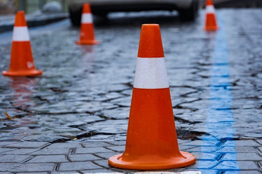 Glimmering rain-soaked cobblestones are lined with vibrant orange traffic cones, indicating ongoing construction while pedestrians carefully navigate through the busy city environment photo