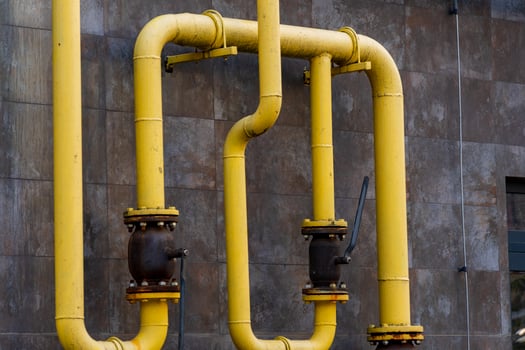 Bright yellow gas pipes wind along a concrete wall, showcasing the intricate connections of energy transportation. Industrial components hint at a complex infrastructure that powers cities photo