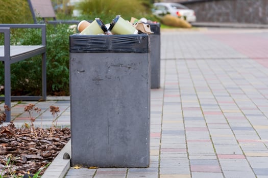 Various garbage containers are overflowing with trash bags, positioned along a clean urban walkway. The scene highlights the importance of proper waste disposal and recycling practices photo