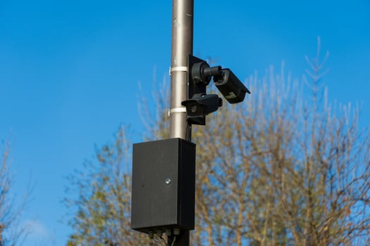 CCTV cameras are securely mounted on metal poles, actively monitoring the surroundings in an outdoor area surrounded by trees, during clear blue sky daylight conditions photo