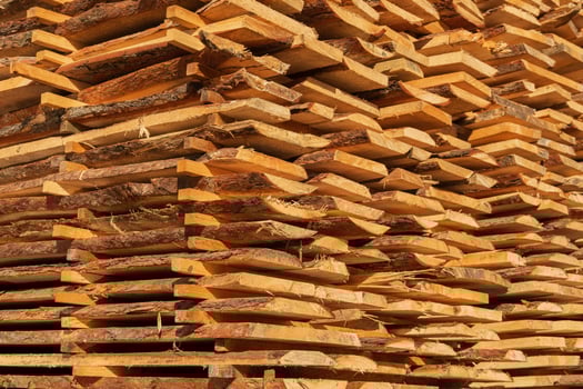 Sunlight filters through wooden stacks at a sawmill, revealing freshly cut timber planks arranged neatly. The warm tones of the wood highlight the texture, showcasing quality lumber photo