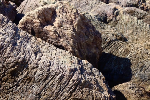 Textured coastal rocks with deep grooves and layers, shaped by centuries of wind and water erosion. The rugged surface contrasts with the soft shadows and sunlight. photo