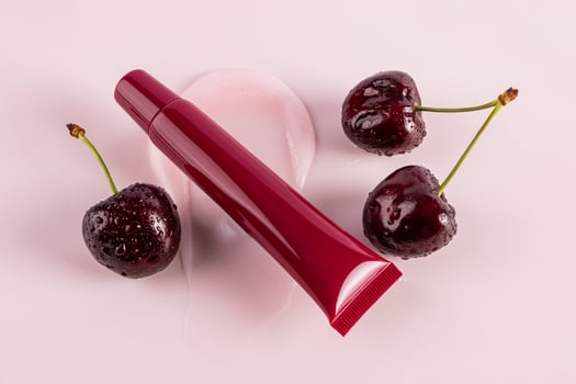 Cosmetic packaging A tube of cherry lip balm lies on a balm sample among ripe cherries. top view. Blank packaging layout. pink background. photo