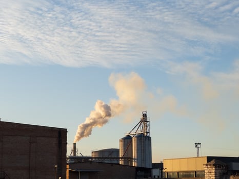The soft hues of dawn illuminate an industrial area where silos stand tall, releasing gentle clouds of smoke into the crisp morning sky photo