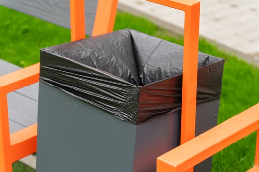 A contemporary trash bin features an elegant black liner, seamlessly integrated with orange seating in a lush green park, inviting visitors to enjoy the fresh air photo