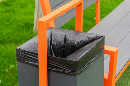 In a lush green park, a contemporary bench with orange accents showcases an attached trash bin, inviting visitors to enjoy the outdoors while keeping the area clean and tidy photo