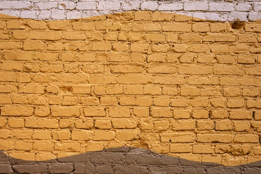 A white brick wall is adorned with a wide yellow wave of paint. The bold contrast creates a striking decorative accent. photo