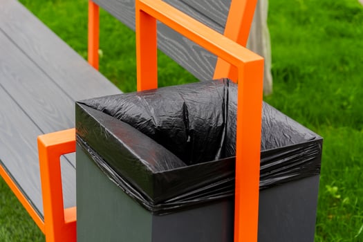 A modern bench featuring a built-in garbage container with a black liner sits on lush green grass, showcasing an aesthetic approach to waste management in public spaces photo