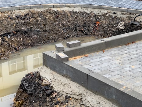 Workers are in the process of laying new pavement near a construction site where drainage problems have created a muddy area and exposed soil around the edges photo
