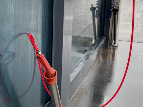A high-pressure car washer gun stands ready for use at a self-service washing station, with droplets of water still glistening on the surface nearby photo