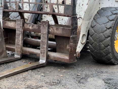 The small loader is positioned on a gravel surface, ready to engage in excavation activities, with its forks visible photo