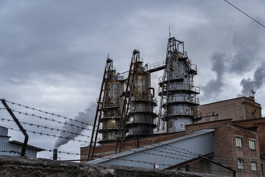 Thick smoke is released from the tall smokestacks of an industrial facility, indicating ongoing production. The sky is overcast, adding to the somber atmosphere photo