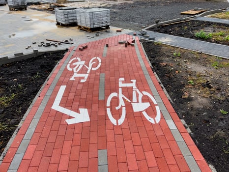 A bike lane sign is prominently displayed on a newly paved red brick path. Construction materials are scattered nearby, indicating ongoing development in the area photo