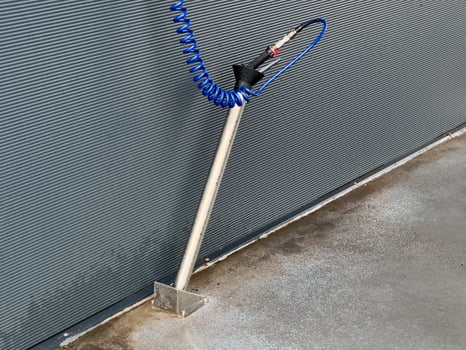 A high-pressure car washer gun stands ready at a car wash location, with a coiled hose extending neatly. This equipment is essential for thorough vehicle cleaning photo