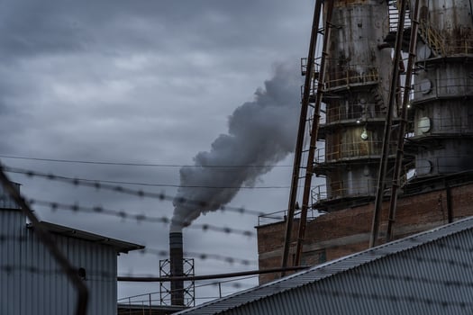 The factory features a tall structure with a brick exterior and rusted supports, releasing dense smoke into the overcast atmosphere, reflecting industrial activity photo