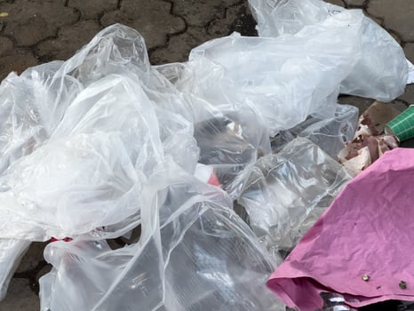 A pile of plastic bags and plastic wrap on the ground. The bags are white and the wrap is clear. The scene is messy and disorganized photo