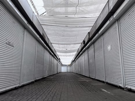 An empty market alley features rows of closed metal shutters under a protective canopy. The atmosphere is quiet, suggesting a peaceful but abandoned space during the morning photo