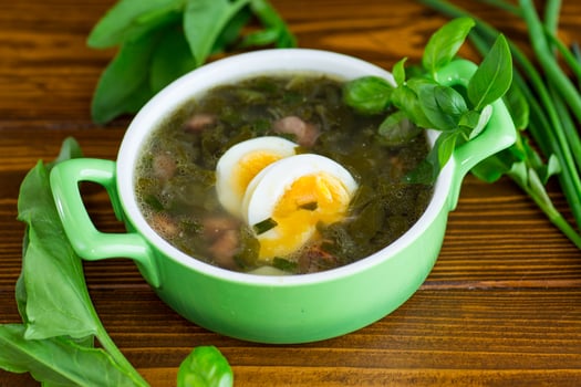 Top view of a plate of green borscht with egg and sorrel on a dark wooden table photo