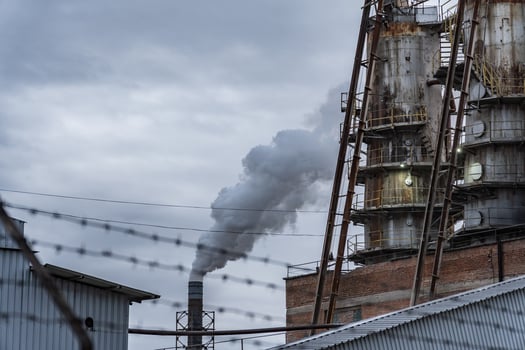A manufacturing facility features large smokestacks that emit gray smoke against a cloudy sky, highlighting industrial activity and environmental impact photo