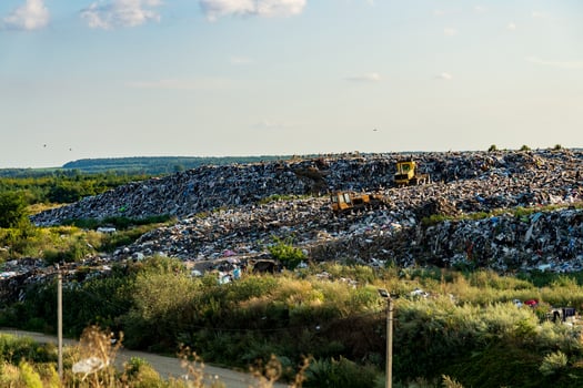 Mountains of refuse accumulate at a landfill site surrounded by greenery, highlighting the environmental impact of waste management practices under the afternoon sun photo