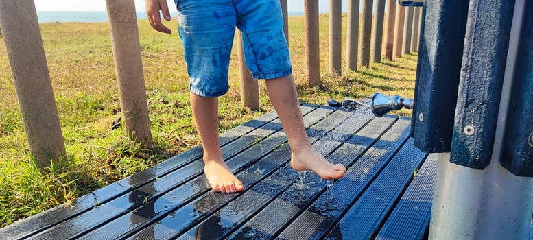 a Boy, toddler washes his feet from sand under the shower on the beach of Portugal close-up. Concept of summer, beach vacation with a child photo